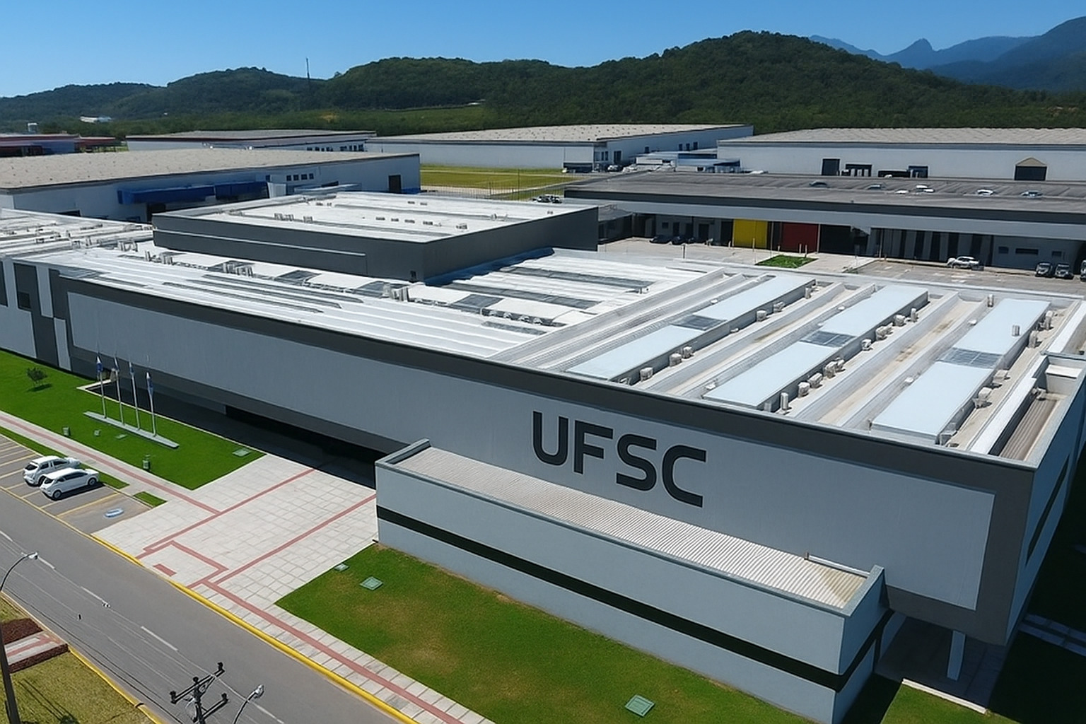 Vista aérea do campus da UFSC ao meio-dia com iluminação intensa e carros estacionados em frente ao prédio principal.