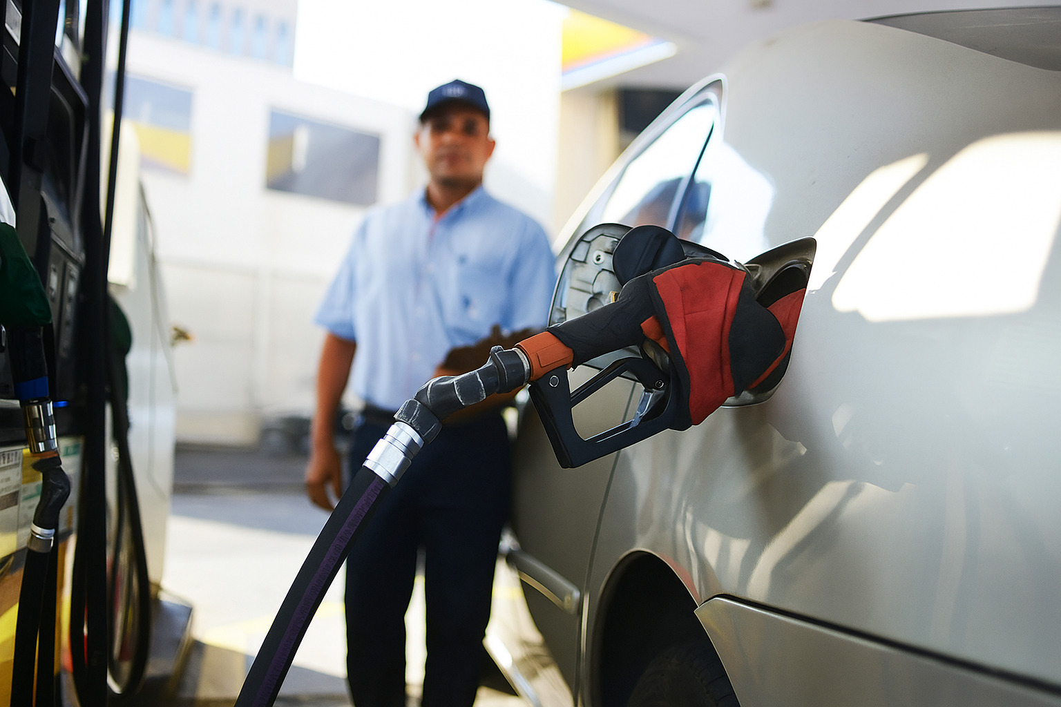 Frentista abastecendo carro prata em posto de combustíveis