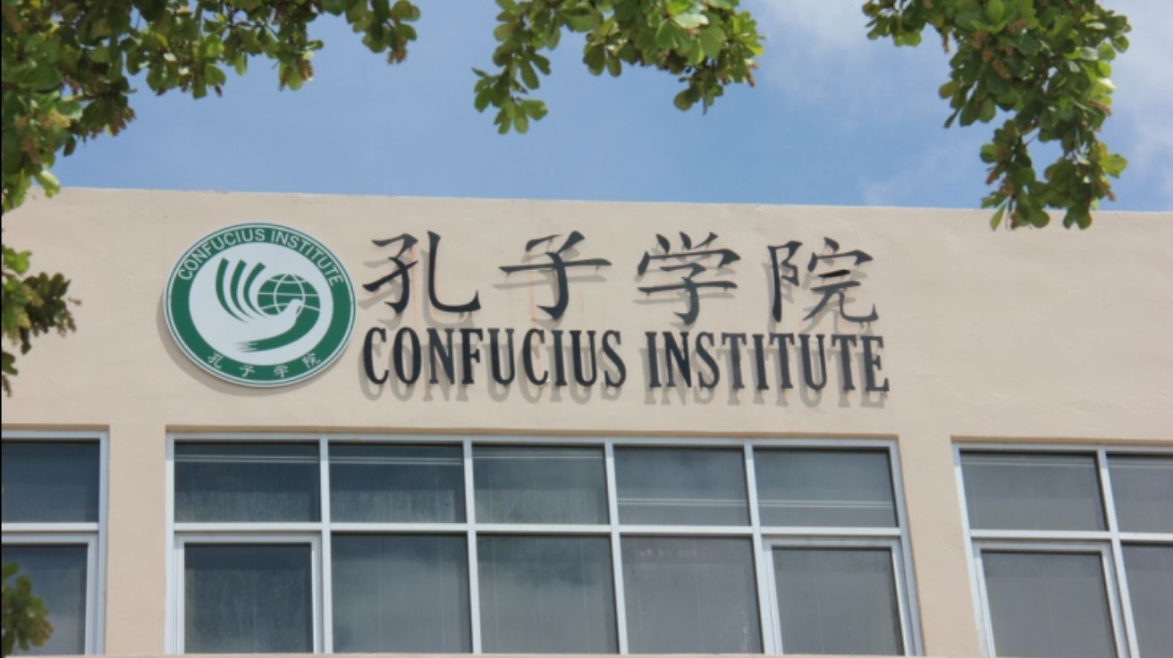 Logotipo e nome do Instituto Confúcio em fachada de prédio universitário com céu azul e árvores ao redor