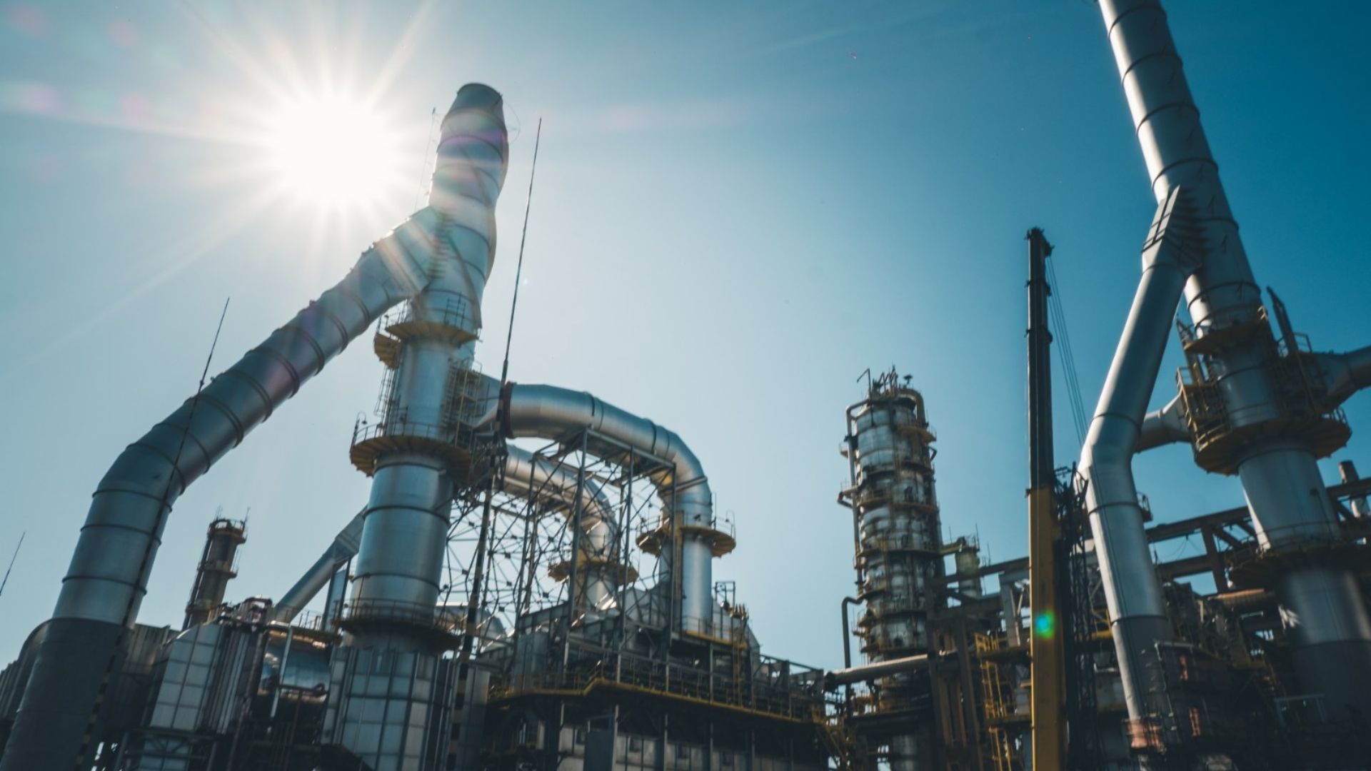 Planta industrial de refino da Petrobras com estruturas metálicas e dutos sob o sol, representando alta eficiência operacional e produção de combustíveis mais limpos no Brasil.