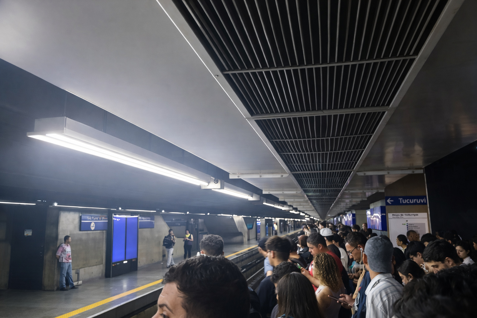 Plataforma da estação do metrô com passageiros aguardando o trem sob iluminação corrigida.